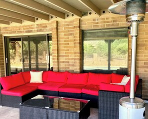 A covered outdoor seating area with a red sectional sofa and a glass-top coffee table.