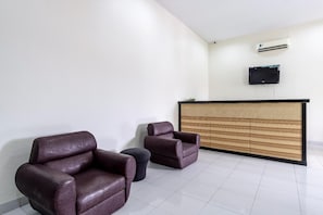 Zona de recepción con mostrador, dos sillones de cuero, un otoman redondo pequeño y un televisor de pantalla plana montado en la pared.