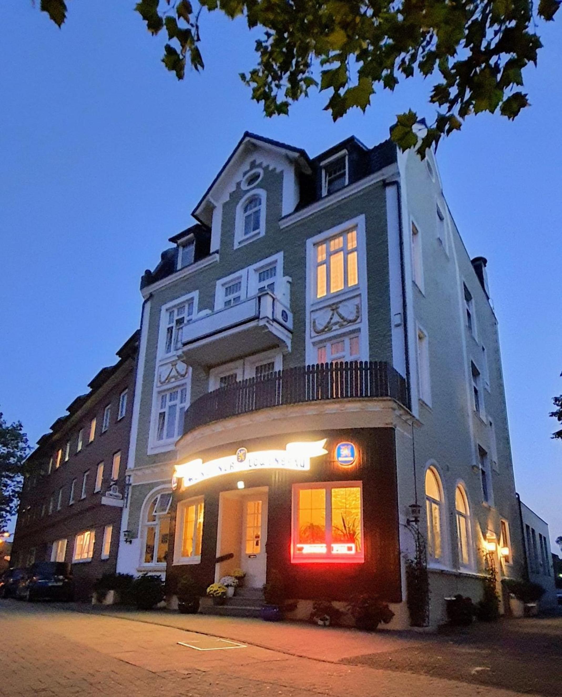 Ein mehrstöckiges Gebäude mit einem Balkon im zweiten Stock, einem beleuchteten Geschäft und einem klaren Himmel.