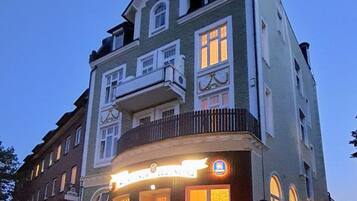 Ein mehrstöckiges Gebäude mit einem Balkon im zweiten Stock, einem beleuchteten Geschäft und einem klaren Himmel.