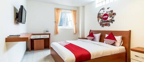 A bedroom with a bed, a desk, a chair, a television, and a window with curtains.
