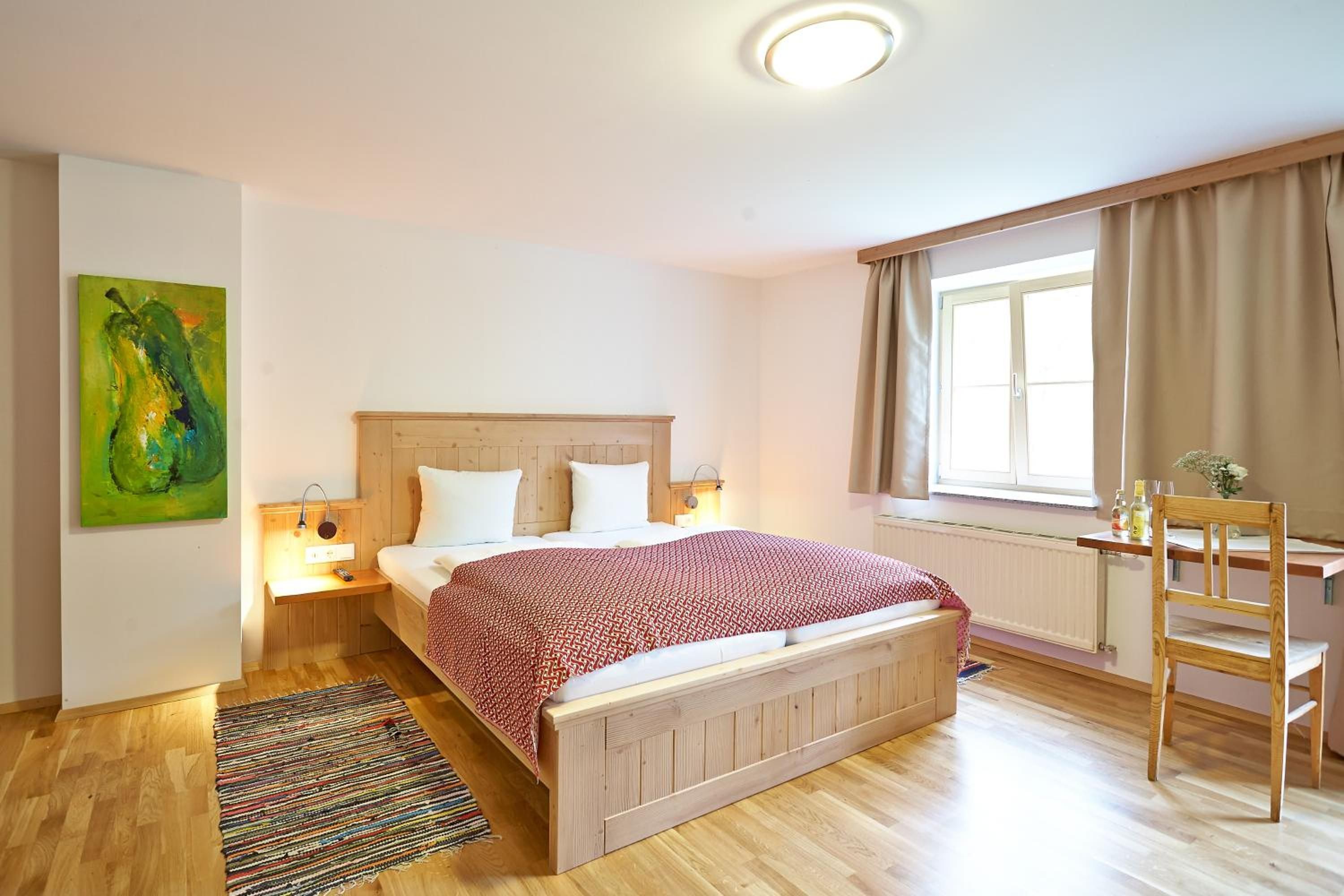 Un dormitorio con cama de madera, lámparas de noche, una ventana con cortinas, un escritorio con silla y una alfombra colorida.