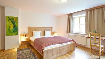 Ein Schlafzimmer mit einem hölzernen Bett, Nachttischlampen, einem Fenster mit Vorhängen, einem Schreibtisch mit Stuhl und einem farbenfrohen Teppich.