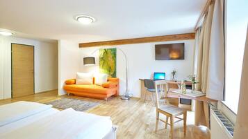 A hotel room with a bed, a desk with a computer, a sofa, and a painting on the wall.
