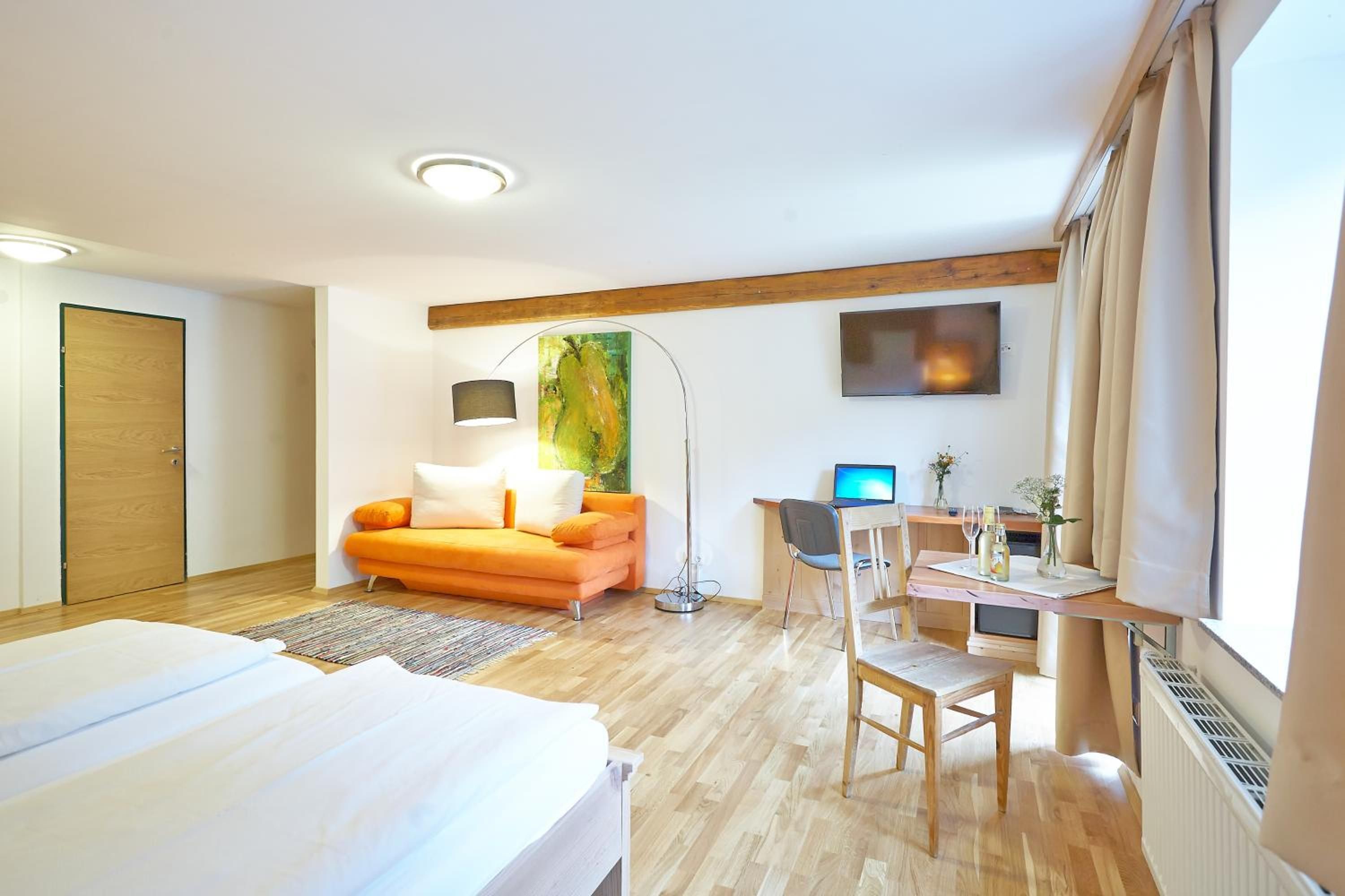 Ein Hotelzimmer mit einem Bett, einem Schreibtisch mit Computer, einer Couch und einem Bild an der Wand.