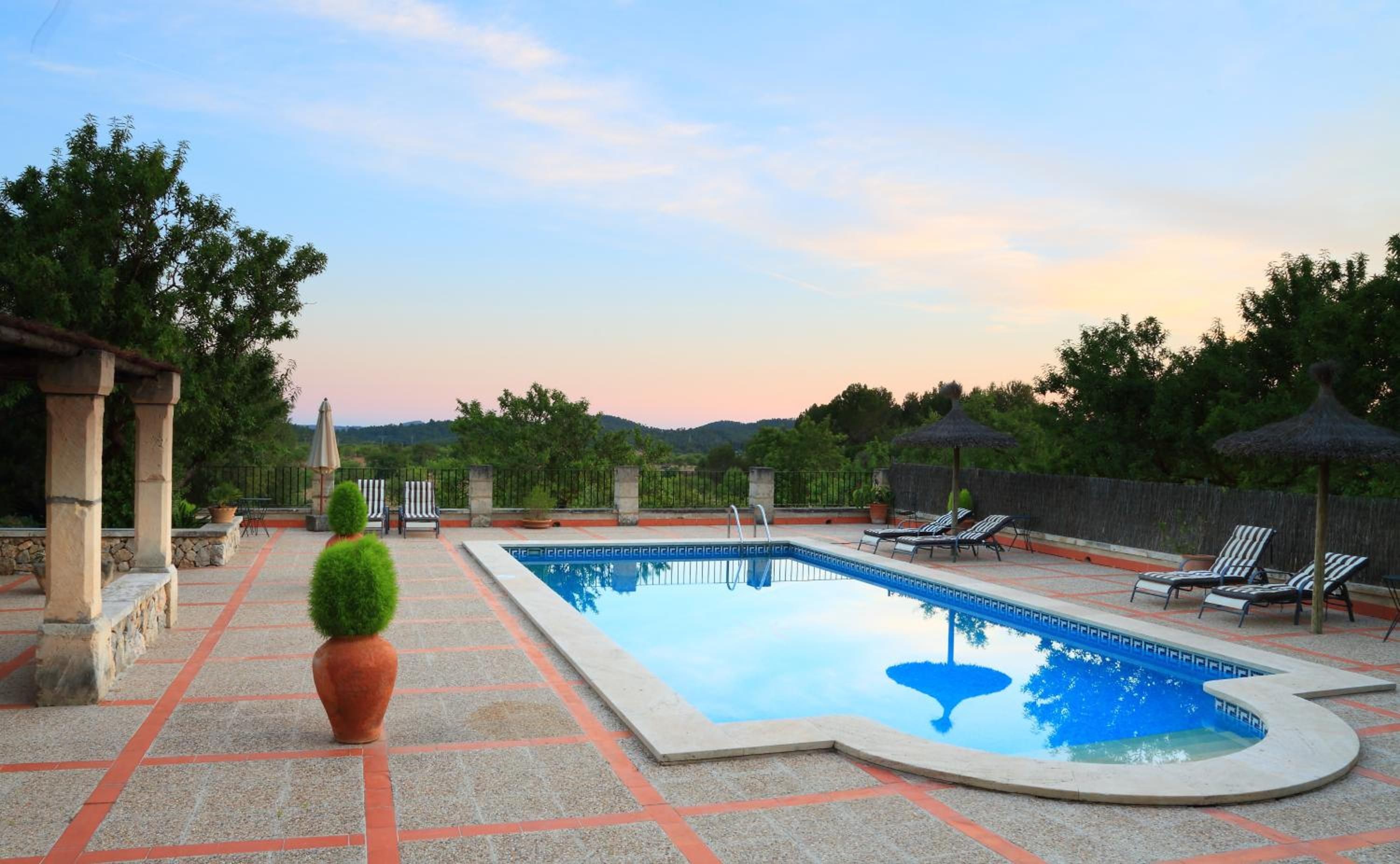 Una piscina con sillas de descanso y sombrillas, rodeada de pilares de piedra y plantas en macetas.