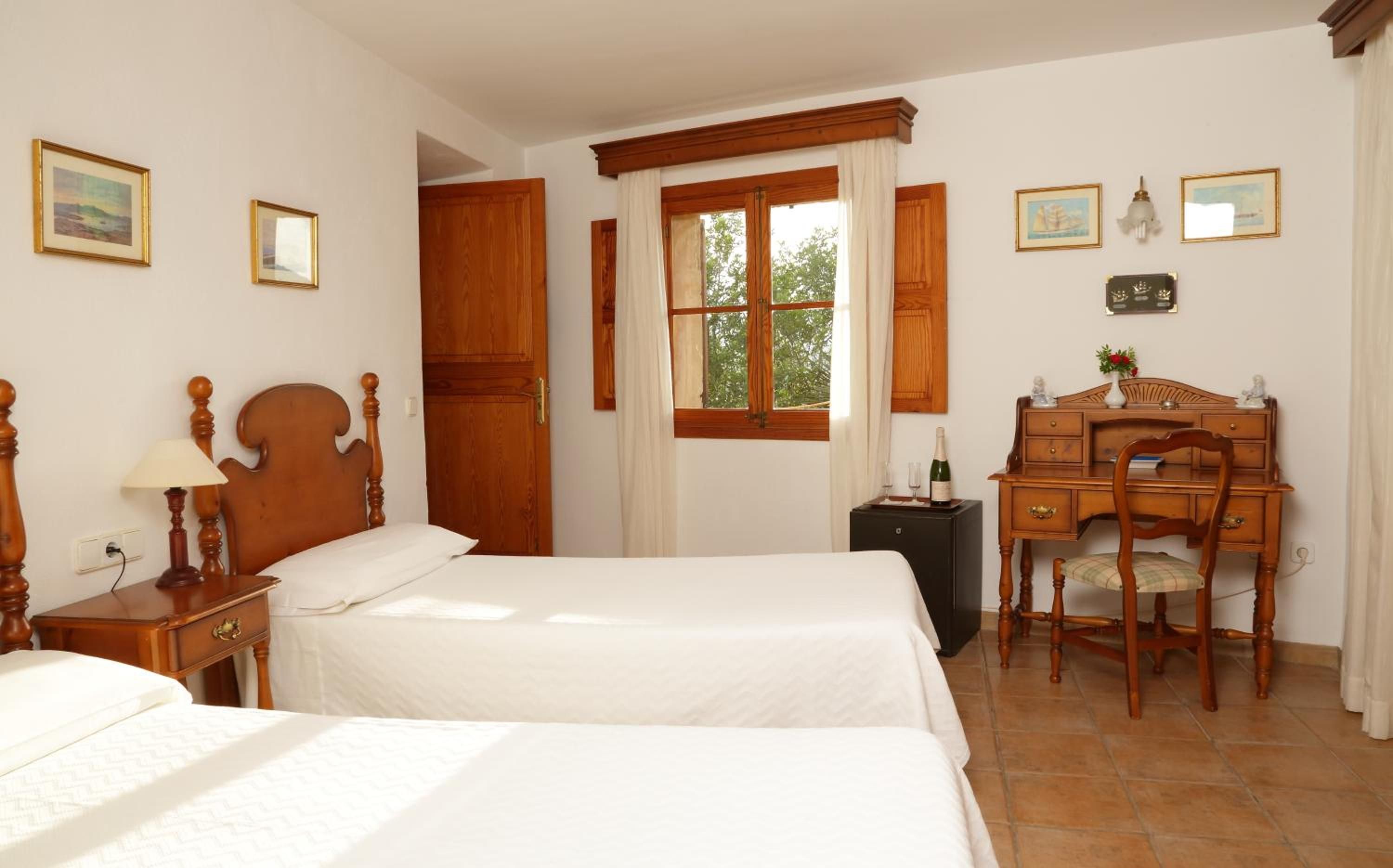 Habitación de hotel con dos camas, un escritorio de madera, una silla y una ventana con cortinas.