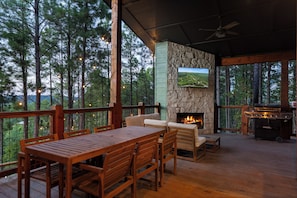 A covered outdoor seating area with a stone fireplace, a television mounted on the wall, and a grill. - NEW Bigfoot Views | Sleeps 18 • Games • Playground (Broken Bow)