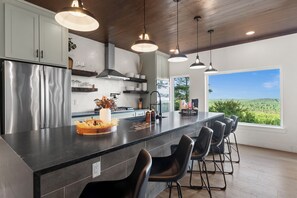 A modern kitchen with a large island, bar stools, and a view of the outdoors. - NEW Bigfoot Views | Sleeps 18 • Games • Playground (Broken Bow)