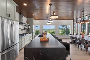 A modern kitchen with a central island, stainless steel appliances, and large windows offering a view of the outdoors. - NEW Bigfoot Views | Sleeps 18 • Games • Playground (Broken Bow)