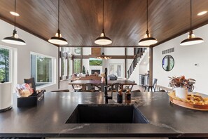 A modern kitchen with a central island, pendant lighting, and a view of the living area. - NEW Bigfoot Views | Sleeps 18 • Games • Playground (Broken Bow)