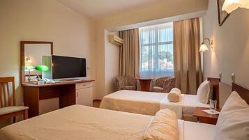 A hotel room with two beds, a desk with a television, a chair, and a window with curtains.