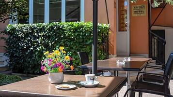 An outdoor seating area with tables, chairs, a flower vase, and a sign for a hotel.