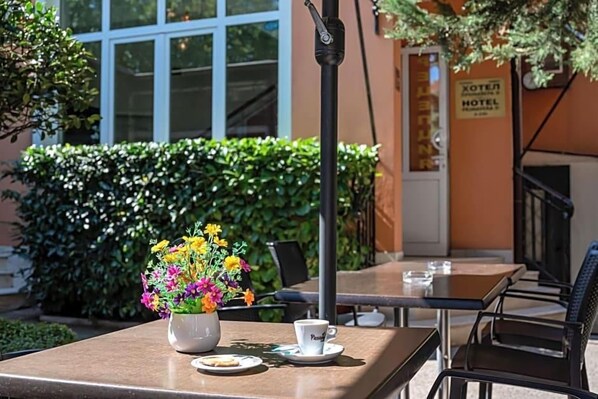 Un área exterior con mesas, sillas, un jarrón de flores y el letrero de un hotel.
