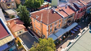 Ein mehrgeschossiges Gebäude mit rotem Ziegeldach, einem zentralen Innenhof und einer straassenseitigen Fassade mit Aussenbestuhlung.