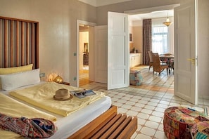 A hotel room with a bed, a bedside table, a chair, and a view of the dining area. - Recknitztal Hotel (Marlow)