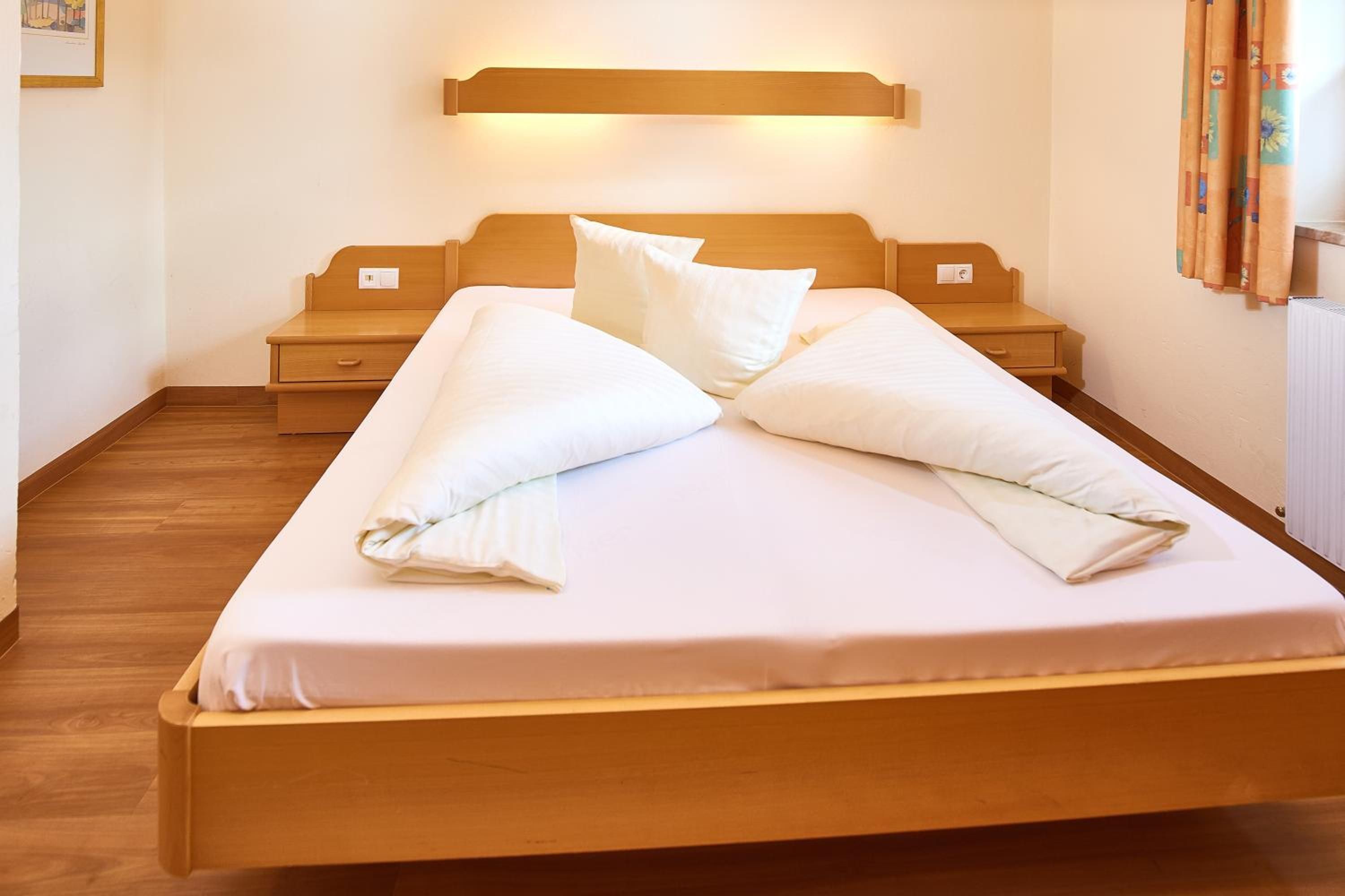 A neatly made bed with pillows, a wooden headboard, and a bedside table with a lamp.