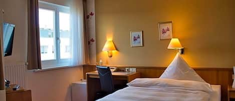 Habitación de hotel con cama, escritorio, silla y televisión a la izquierda.