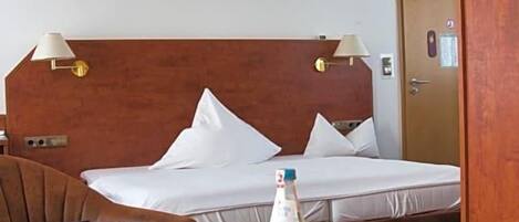 A hotel room with a bed, bedside lamps, a table with a bottle, a glass, and a box.
