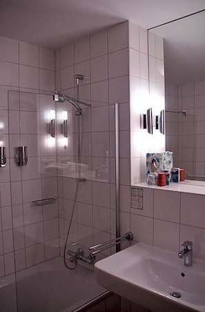 A modern bathroom with a glass-enclosed shower, a sink, and a mirror. - Quellenhof (Salzgitter)