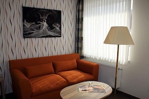 A room with a sofa, a lamp, a radiator, and a painting on the wall. - Quellenhof (Salzgitter)