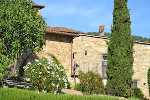 A stone building with a tiled roof, surrounded by greenery and flowering plants.