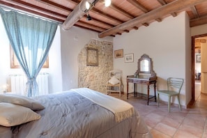 A bedroom with a bed, a desk, a chair, a stone wall, and a mirror. - Vignola Apartments (Pontassieve)