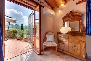 A room with a wooden cabinet, a chair, and a view of a balcony with potted plants. - Vignola Apartments (Pontassieve)