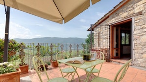 Une terrasse avec une table et des chaises, des plantes en pot et une vue sur la mer et les montagnes.