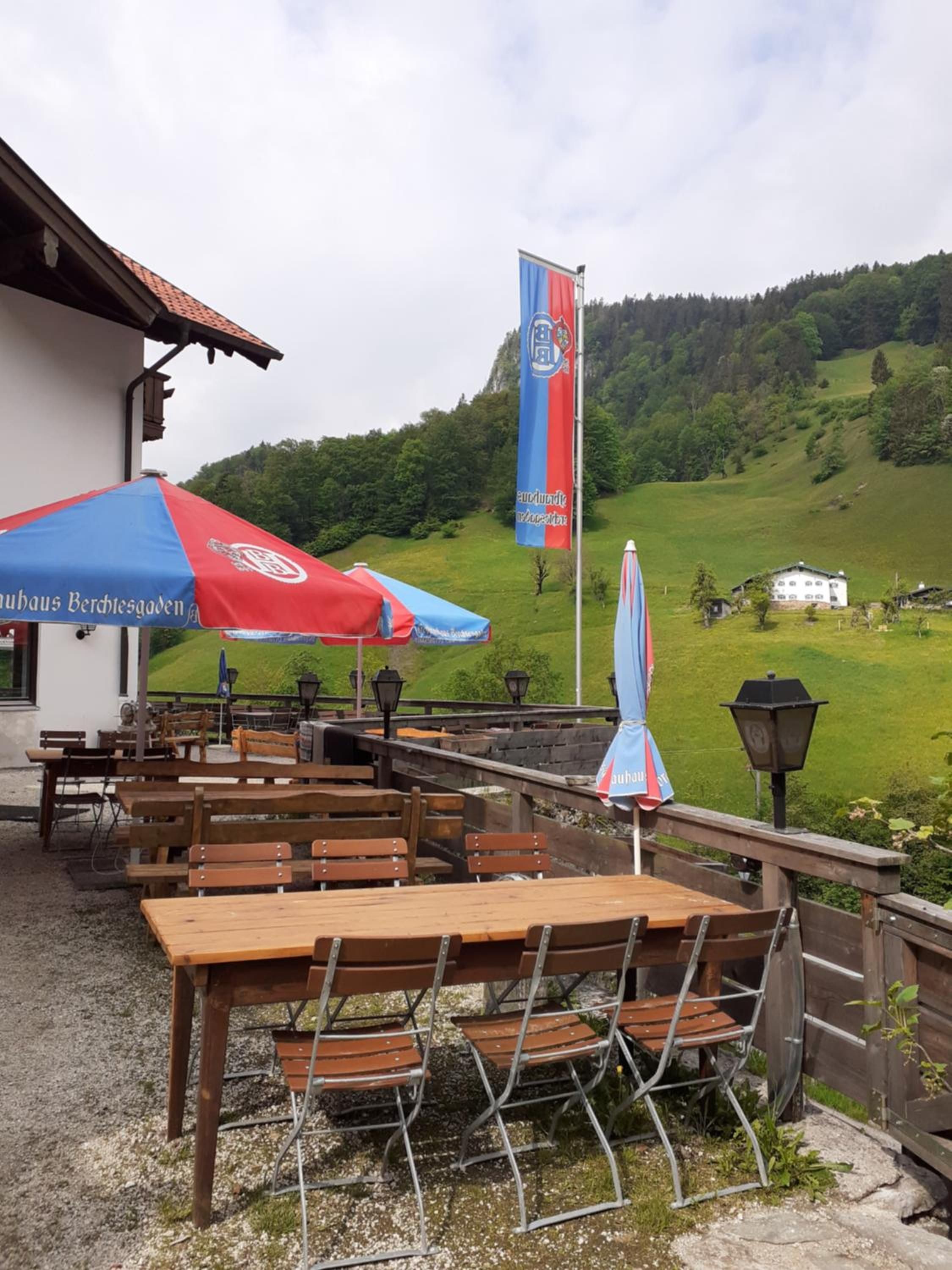 Un espace extérieur aménagé avec des tables et des chaises en bois, un drapeau et une vue sur une colline verdoyante.