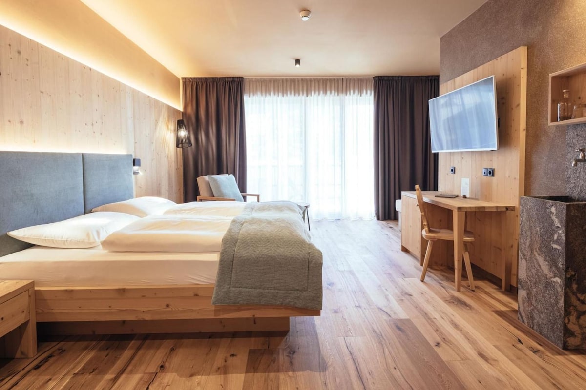 A hotel room with a large bed, a desk, a television, and a stone sink.