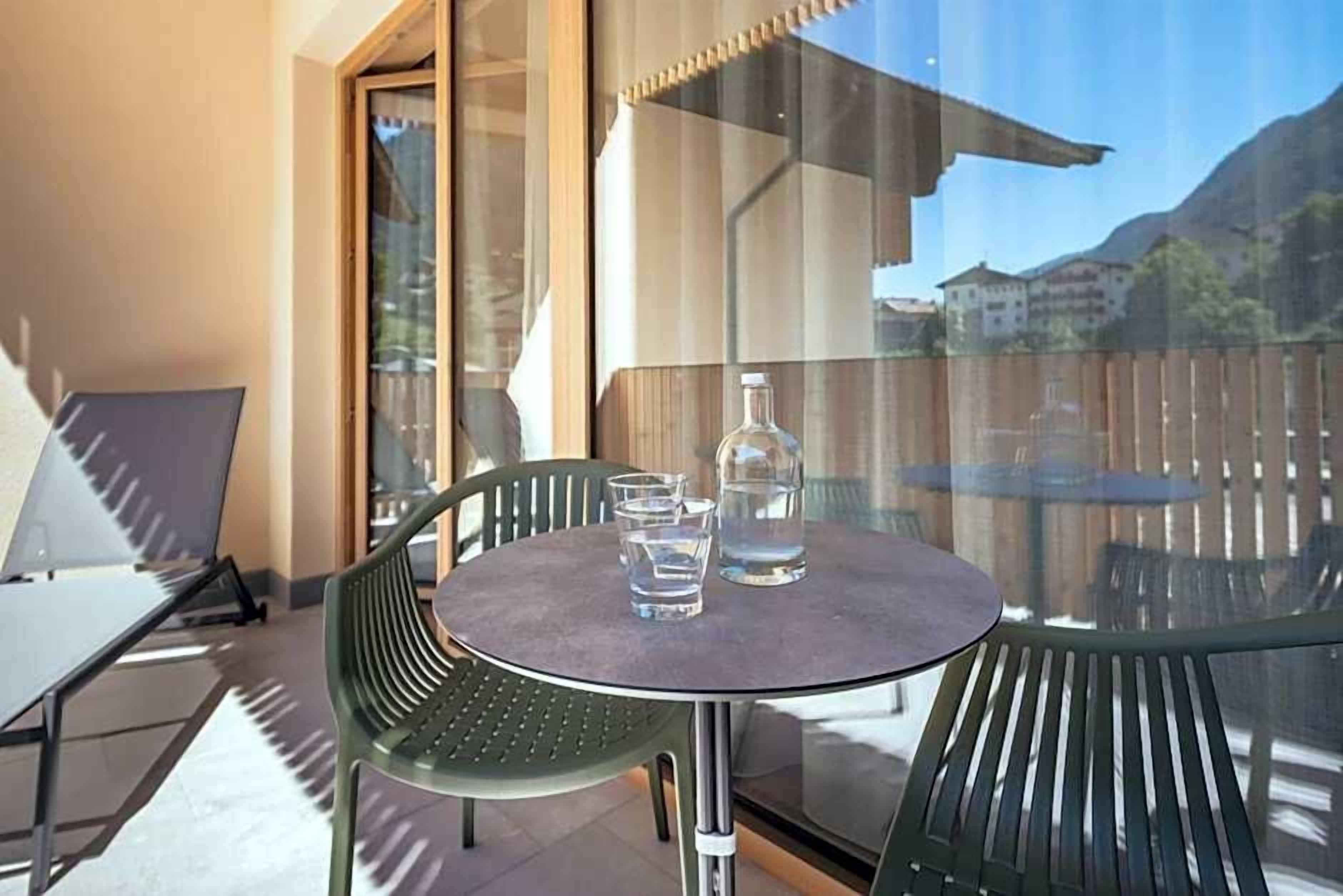 A balcony with a round table, two chairs, a bottle, and glasses.
