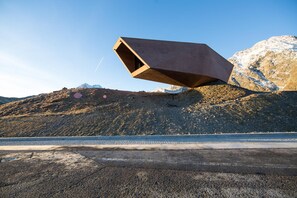 A modern architectural structure with a slanted roof, situated on a hillside with a clear sky. - Tiroler Hof (San Leonardo in Passiria)