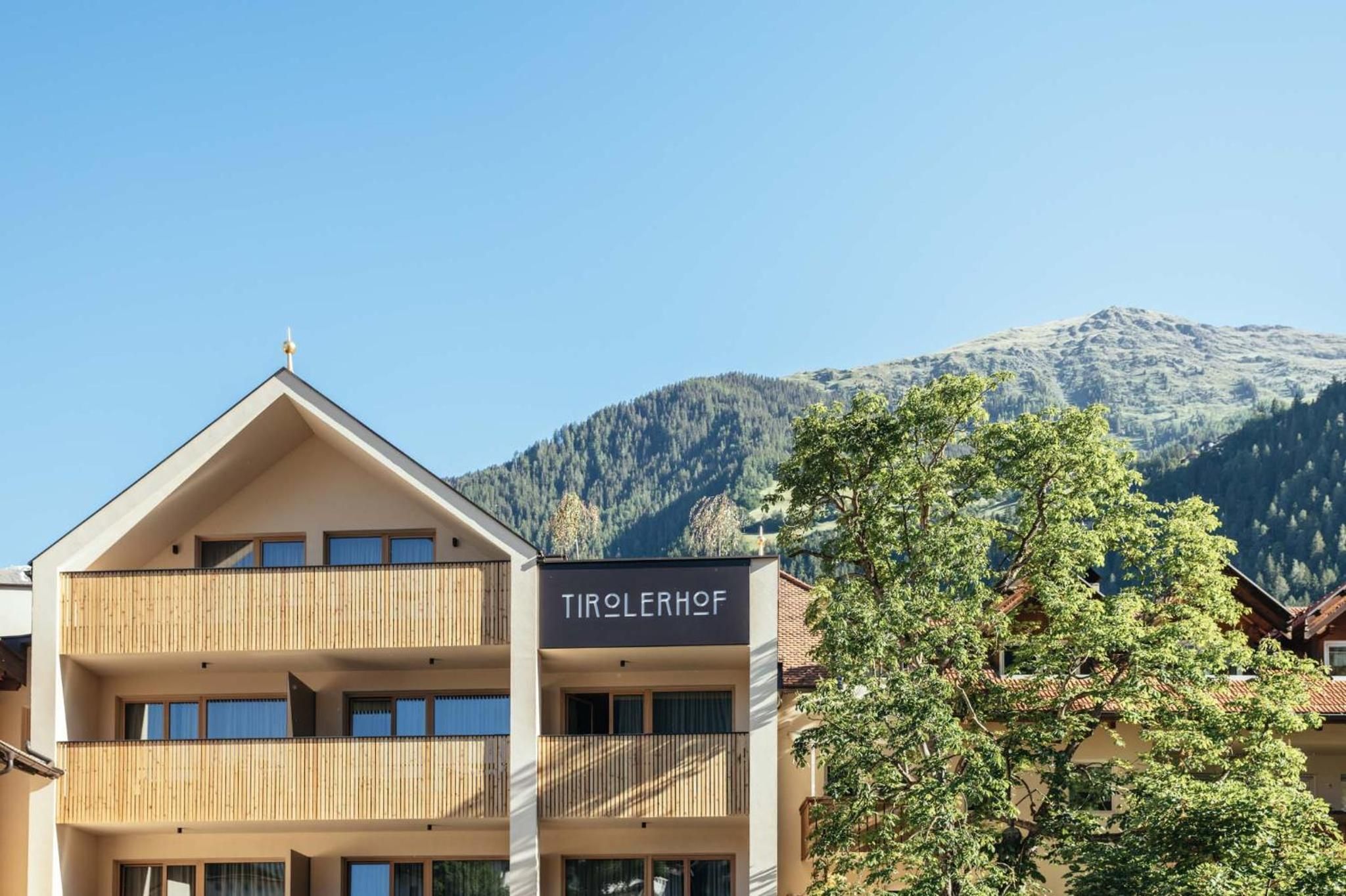 A hotel with a sign reading 'TIROLERHOF' in front of a mountain backdrop.