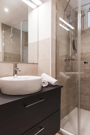 A modern bathroom with a large sink, a mirror, and a glass-enclosed shower area. - Strandhotel Sille (Maria Woerth)
