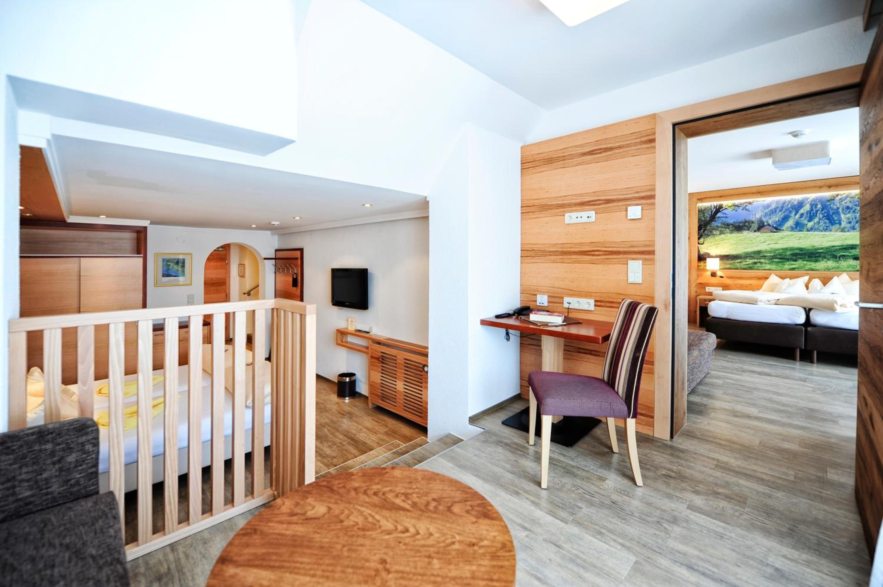 A modern room with a crib, a desk, a chair, and a sofa. There is a large window with a view of a landscape.