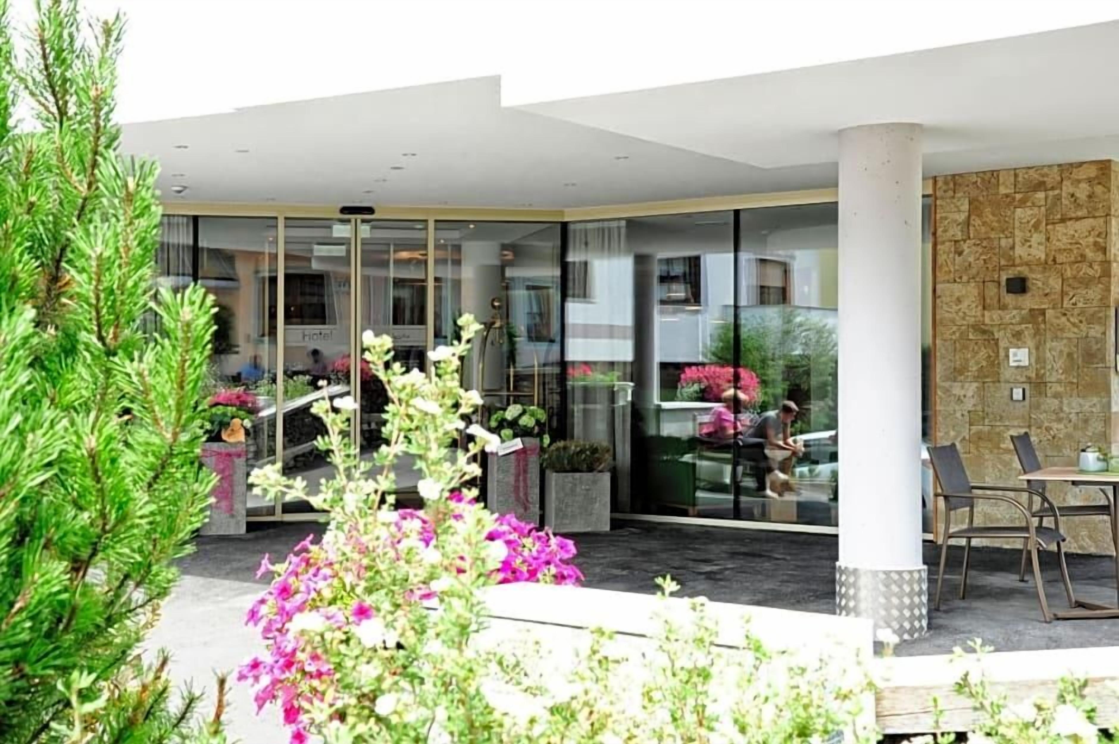 A hotel entrance with a glass door, outdoor seating, and a stone wall.