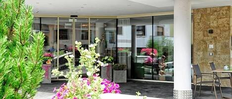 A hotel entrance with a glass door, outdoor seating, and a stone wall.