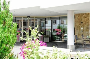 Entrada de hotel con puerta de cristal, asientos exteriores y una pared de piedra.