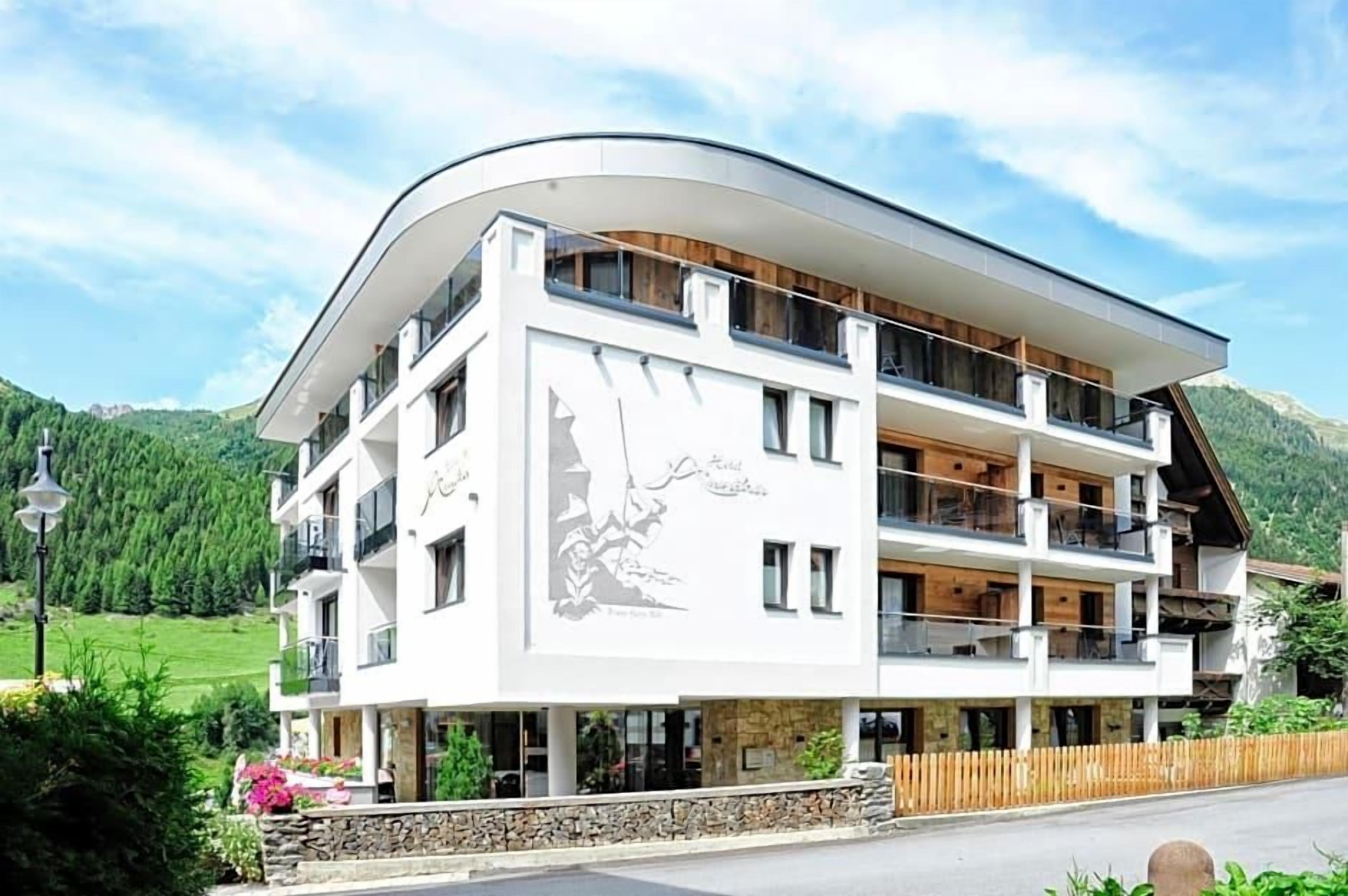 A multi-story hotel with a curved facade, balconies, and a mountainous backdrop.
