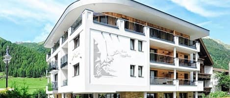 A multi-story hotel with a curved facade, balconies, and a mountainous backdrop.