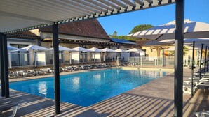 A swimming pool with lounge chairs and umbrellas, surrounded by a covered area with a pergola. - L'oustal (Vezac)