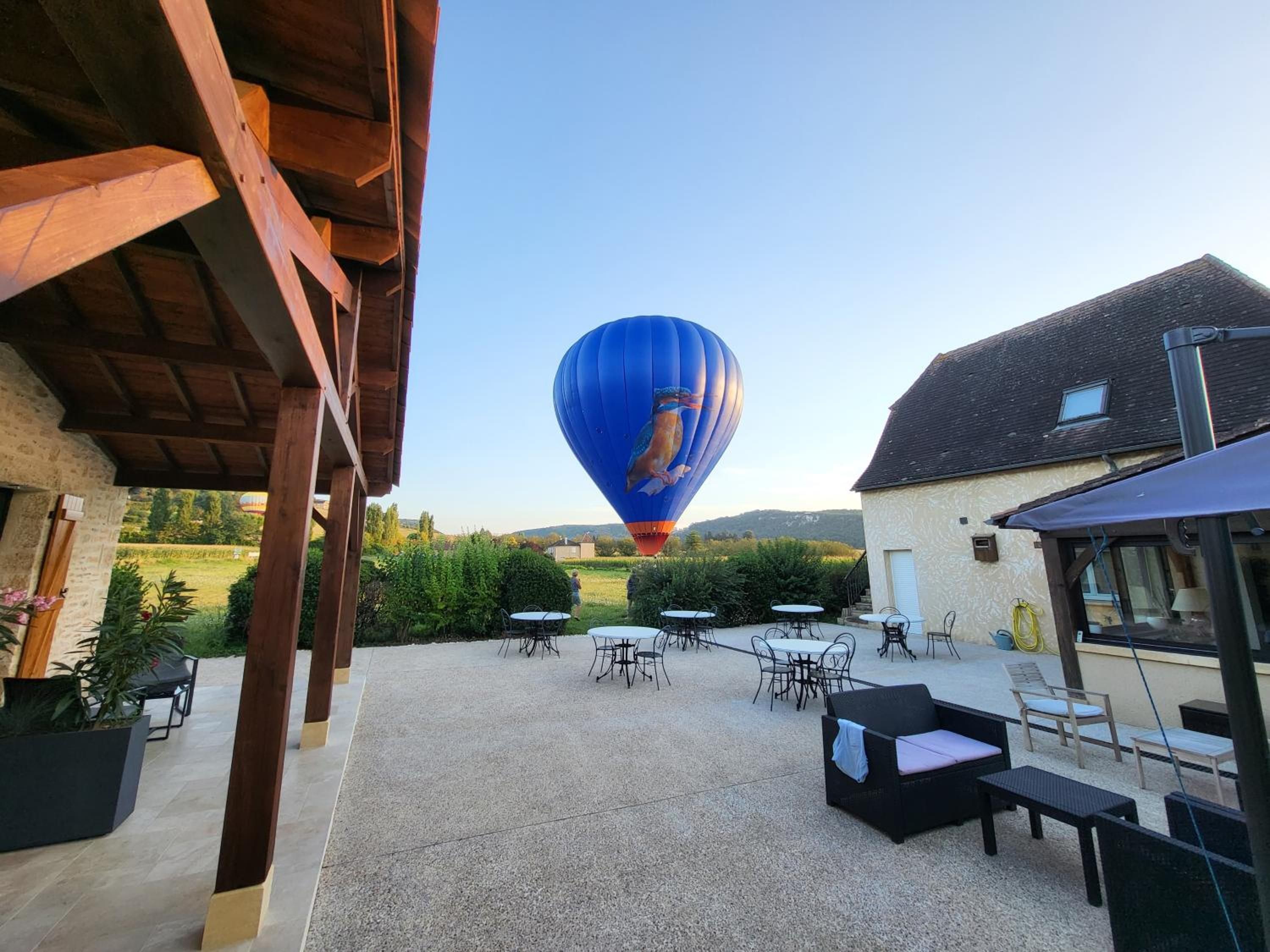 A hot air balloon in the distance, outdoor seating area with tables and chairs, and a building with a sloped roof.