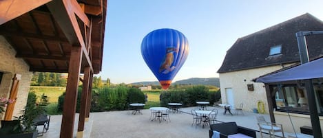 A hot air balloon in the distance, outdoor seating area with tables and chairs, and a building with a sloped roof.