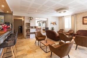 Eine Hotelhalle mit Barbereich, Sitzgelegenheiten, einer Bücherwand und Blick auf die Küche.