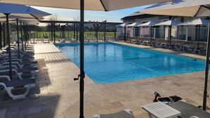 A swimming pool with lounge chairs and umbrellas, surrounded by a tiled deck. - L'oustal (Vezac)