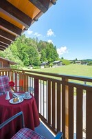 A balcony with a table set for two, overlooking a green landscape with houses.