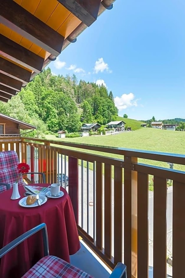 A balcony with a table set for two, overlooking a green landscape with houses. - Bellevue (Mittelberg)
