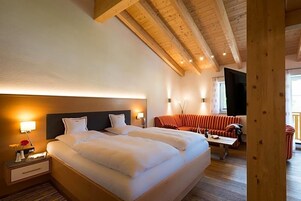 Quarto de hotel com uma cama grande, um sofá e teto de madeira.