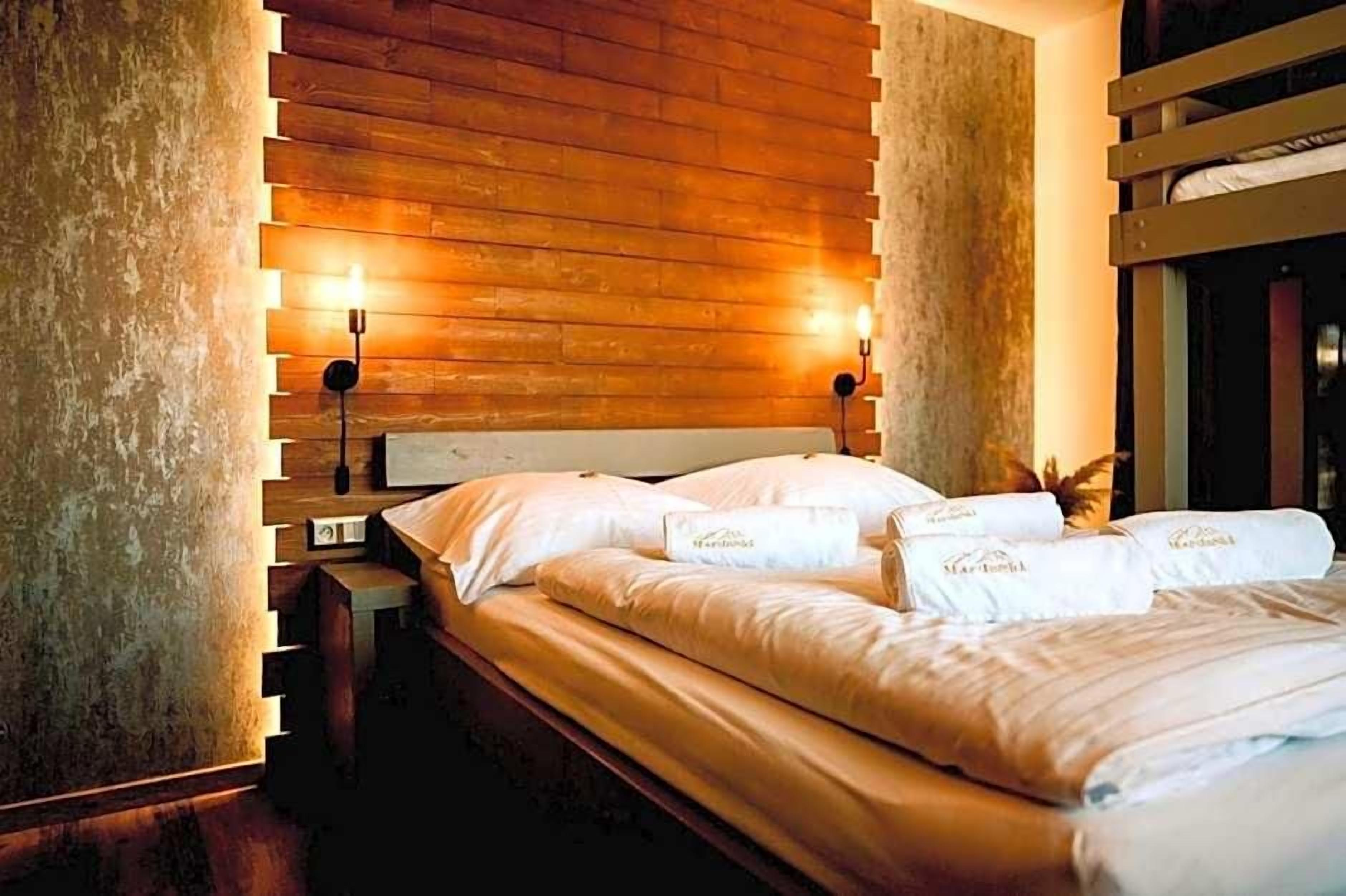 A hotel room with a wooden headboard, a bed with white linens, and two wall-mounted lamps.